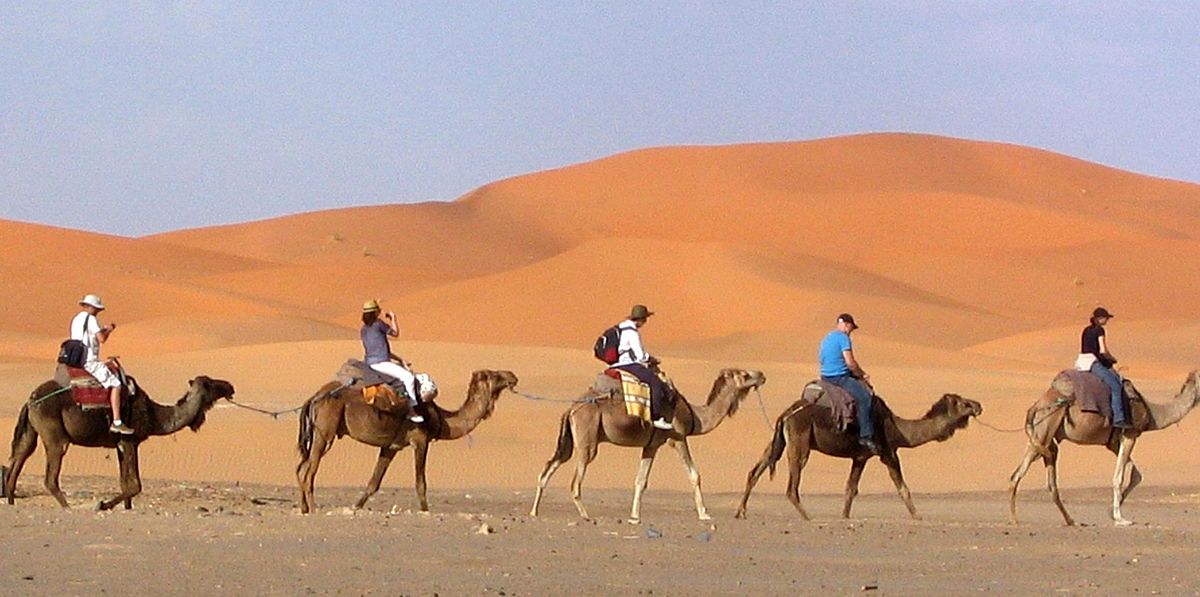 1200px-Tourists_on_a_camel_excursion_into_the_Sahara_desert_near_the_village_of_Mhamid_El_Ghezlane%2C_Morocco.jpg